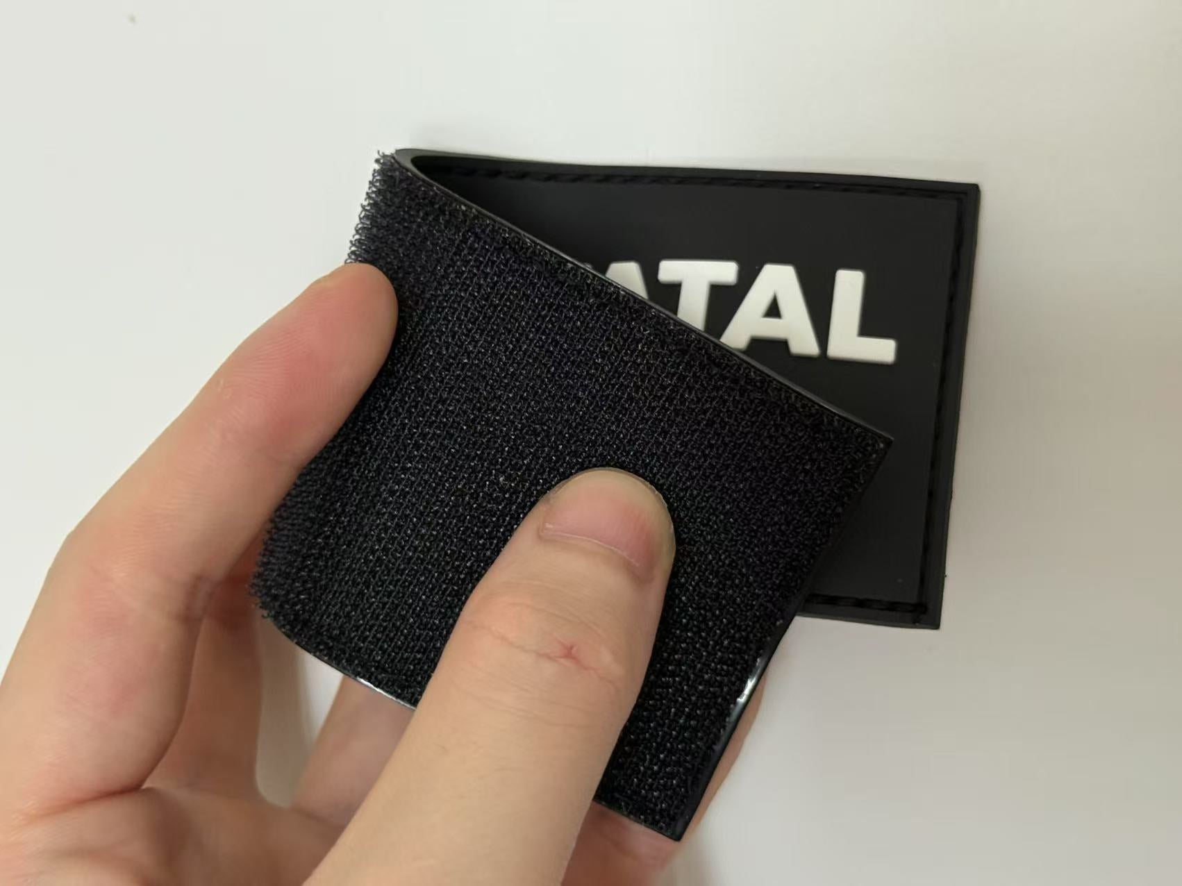 A custom 3D silicone tactical morale patch with a black hook and loop backing, shown next to a backpack